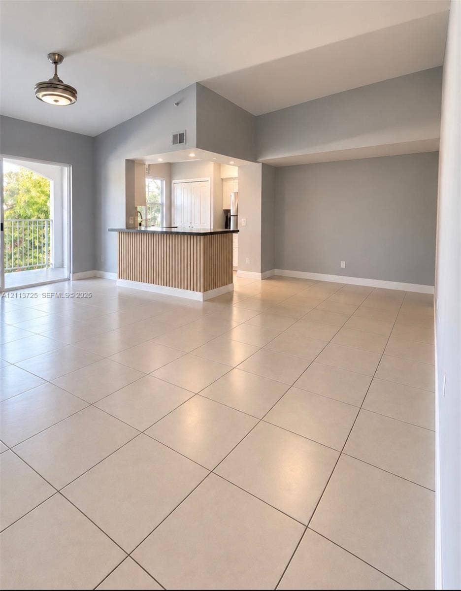 Open living area featuring vaulted ceilings, neutral floor tiling, a slatted wood-finish breakfast bar, and access to a private balcony
