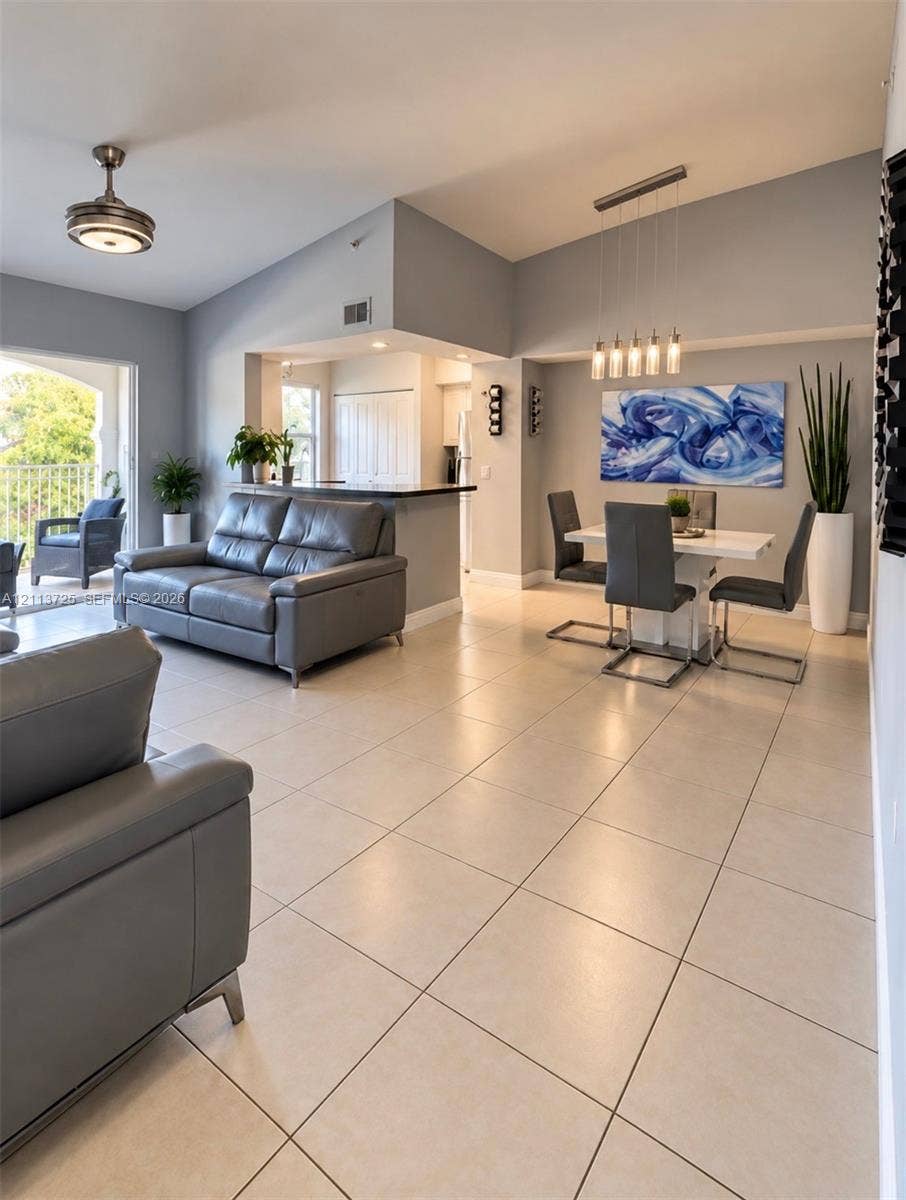 Open-concept interior featuring high vaulted ceilings, neutral large-format tile flooring, a breakfast bar with a dark countertop, and modern multi-pendant lighting