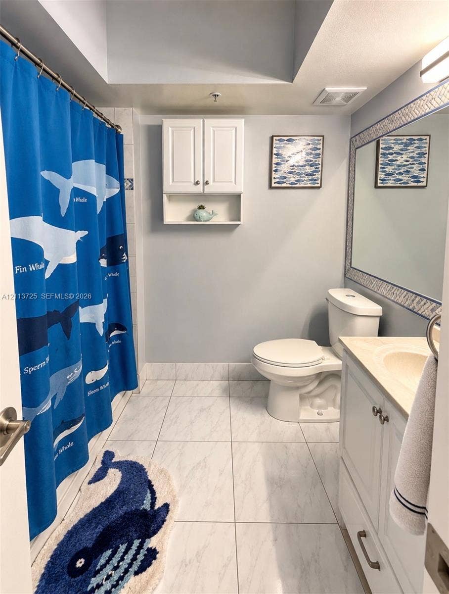 Bathroom featuring tile flooring, white cabinetry, a built-in wall cabinet, and a large wall-mounted mirror with a decorative frame