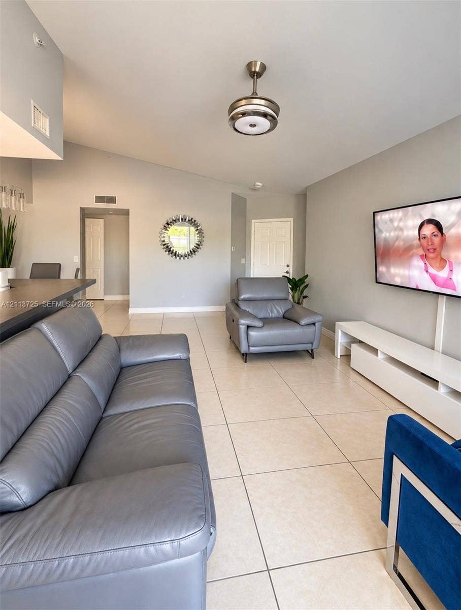 Open-concept interior featuring high sloped ceilings, large format ceramic tile flooring, a breakfast bar with a neutral countertop, and a brushed nickel ceiling fan with integrated lighting