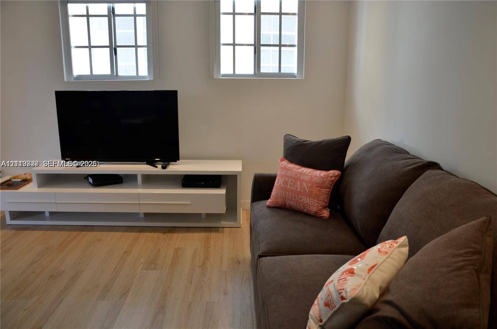 700 SE 16th Street, #201, Miami Beach, Miami Beach, FL 33139 Light-toned wood-finish flooring, two dual-pane windows with grid detailing, and a white built-in media console