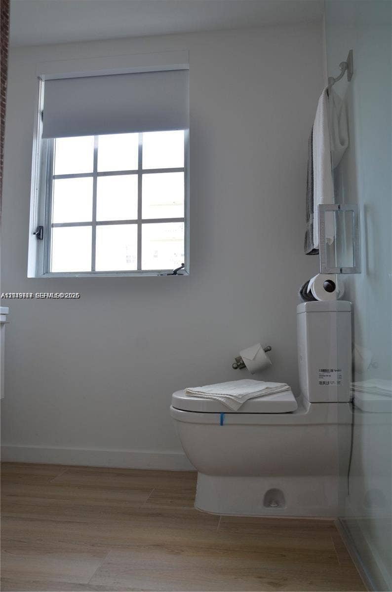 700 SE 16th Street, #201, Miami Beach, Miami Beach, FL 33139 Bathroom featuring a dual-flush toilet, wood-finish flooring, multi-pane window with a roller shade, and wall-mounted hardware