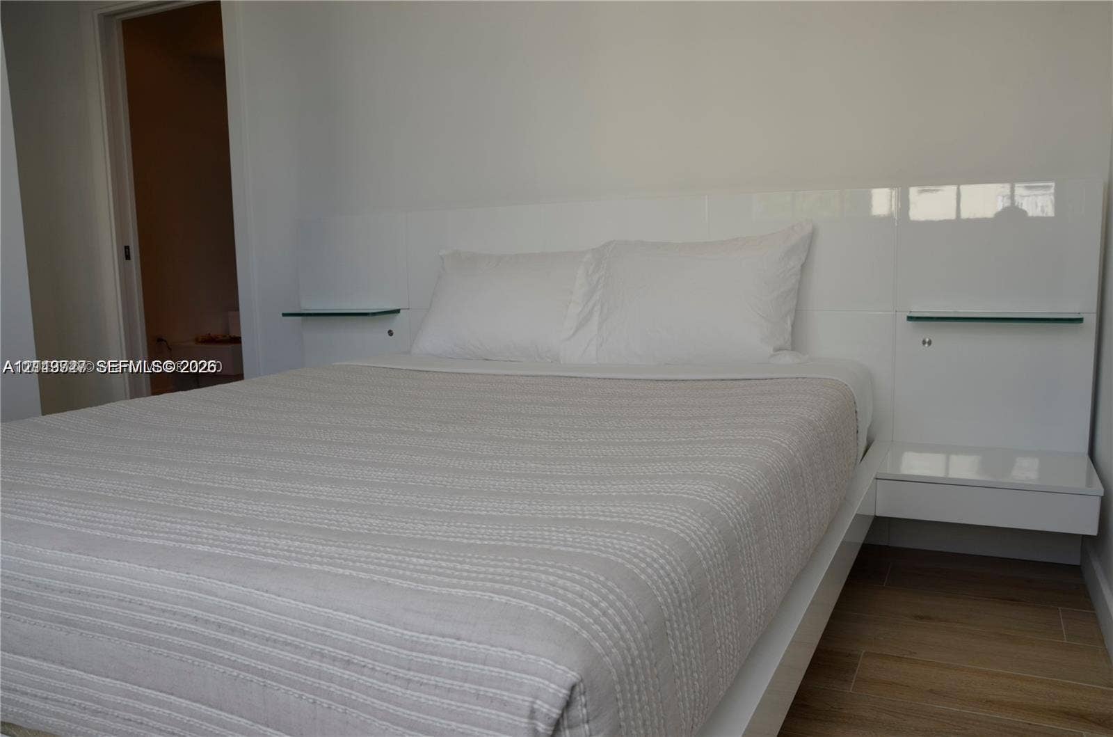 700 SE 16th Street, #201, Miami Beach, Miami Beach, FL 33139 Built-in high-gloss white headboard featuring integrated glass shelving and floating side tables, complemented by wood-finish flooring