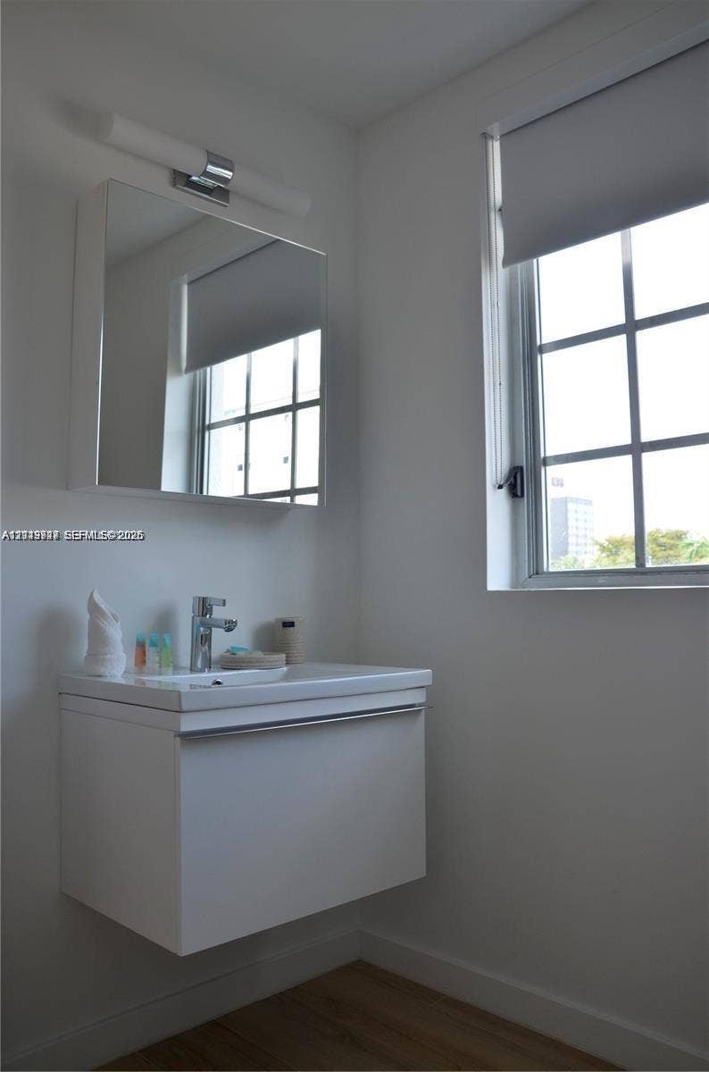 700 SE 16th Street, #201, Miami Beach, Miami Beach, FL 33139 Wall-mounted floating vanity with a integrated basin and chrome single-lever faucet, accompanied by a matching mirrored medicine cabinet, linear wall-mounted lighting fixture, and window with a grid pattern