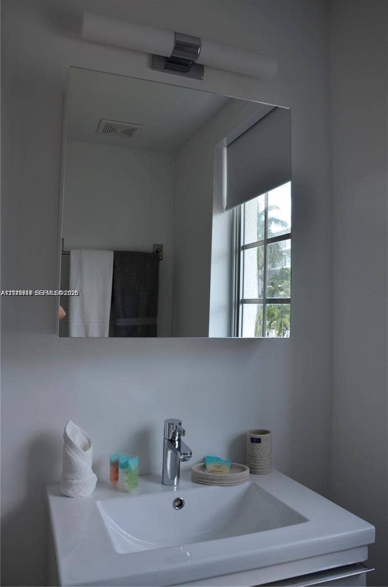 700 SE 16th Street, #201, Miami Beach, Miami Beach, FL 33139 Wall-mounted rectangular mirror featuring a chrome-finished light fixture, integrated sink with a single-handle faucet, and built-in towel hardware