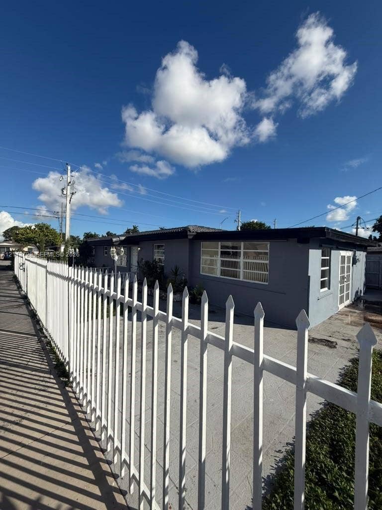 9200 SW 37th Street, Miami, FL 33165 Single-story exterior featuring a white metal picket fence, paved concrete driveway, multi-pane windows, and dual-pane glass entry doors
