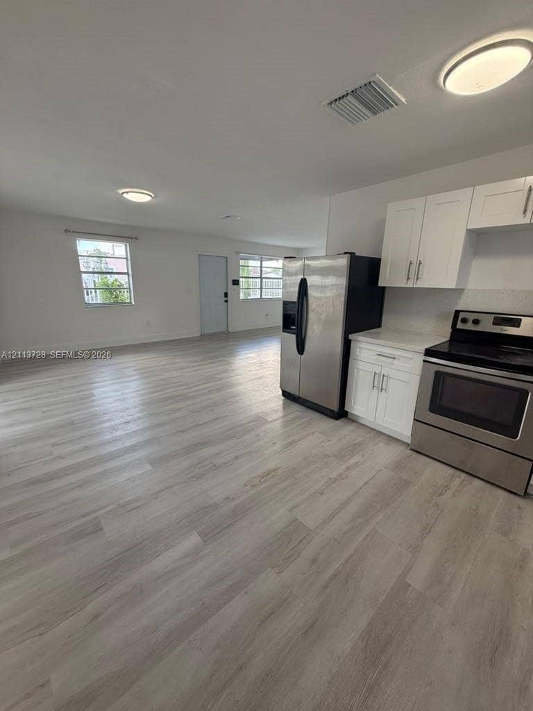 9200 SW 37th Street, Miami, FL 33165 Kitchen featuring shaker-style white cabinetry, stone-finish countertops, and stainless steel appliances, set against wood-finish flooring and flush-mount ceiling lighting