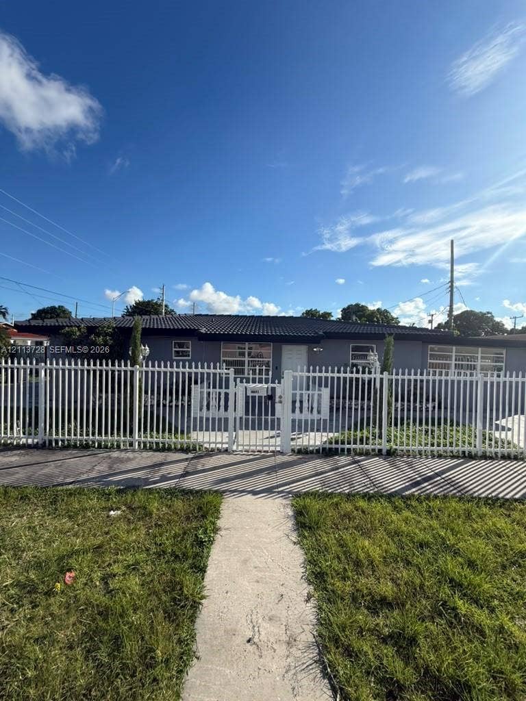 9200 SW 37th Street, Miami, FL 33165 Single-story exterior featuring a dark tile roof, horizontal siding, horizontal-pane windows, and a full-perimeter white metal fence with a gated entrance