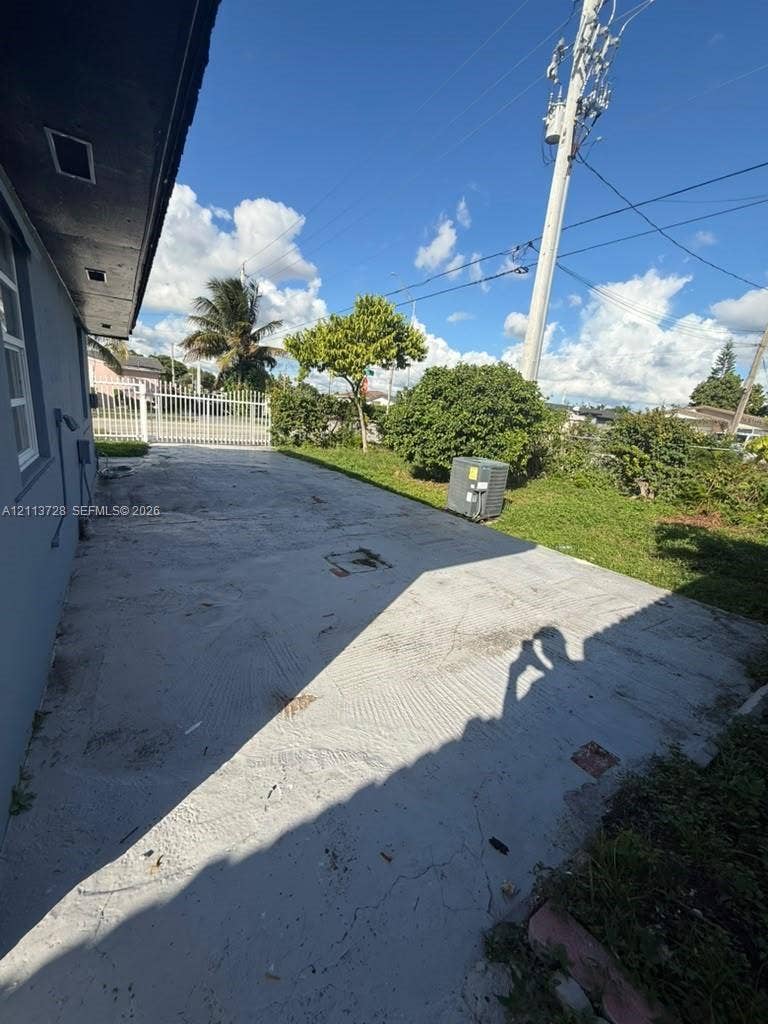 9200 SW 37th Street, Miami, FL 33165 Concrete exterior side yard featuring a white metal gate and mature landscaping