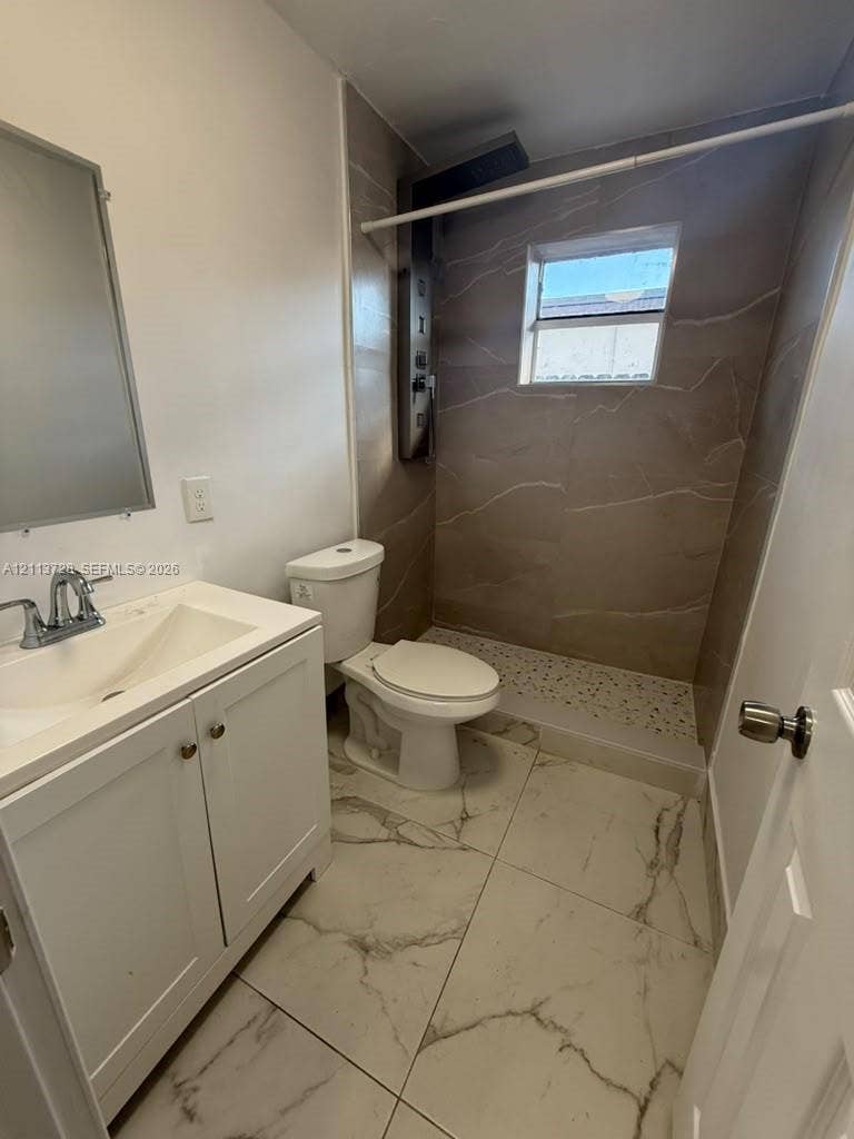 9200 SW 37th Street, Miami, FL 33165 Bathroom featuring oversized floor tiles with stone-patterned veining, white vanity cabinet with a integrated sink, and a walk-in shower with large-format wall tiling and a pebble-texture floor base