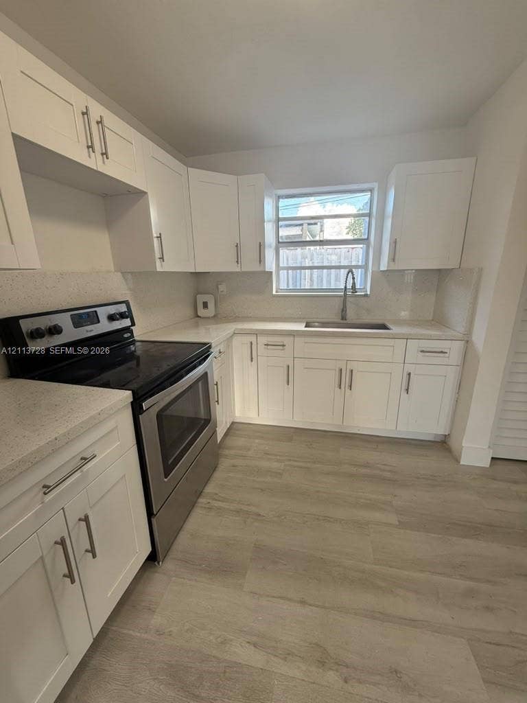 9200 SW 37th Street, Miami, FL 33165 Kitchen featuring white Shaker-style cabinetry, light-toned stone-finish countertops, stainless steel appliances, wood-finish flooring, and a single-basin undermount sink with a pull-down faucet