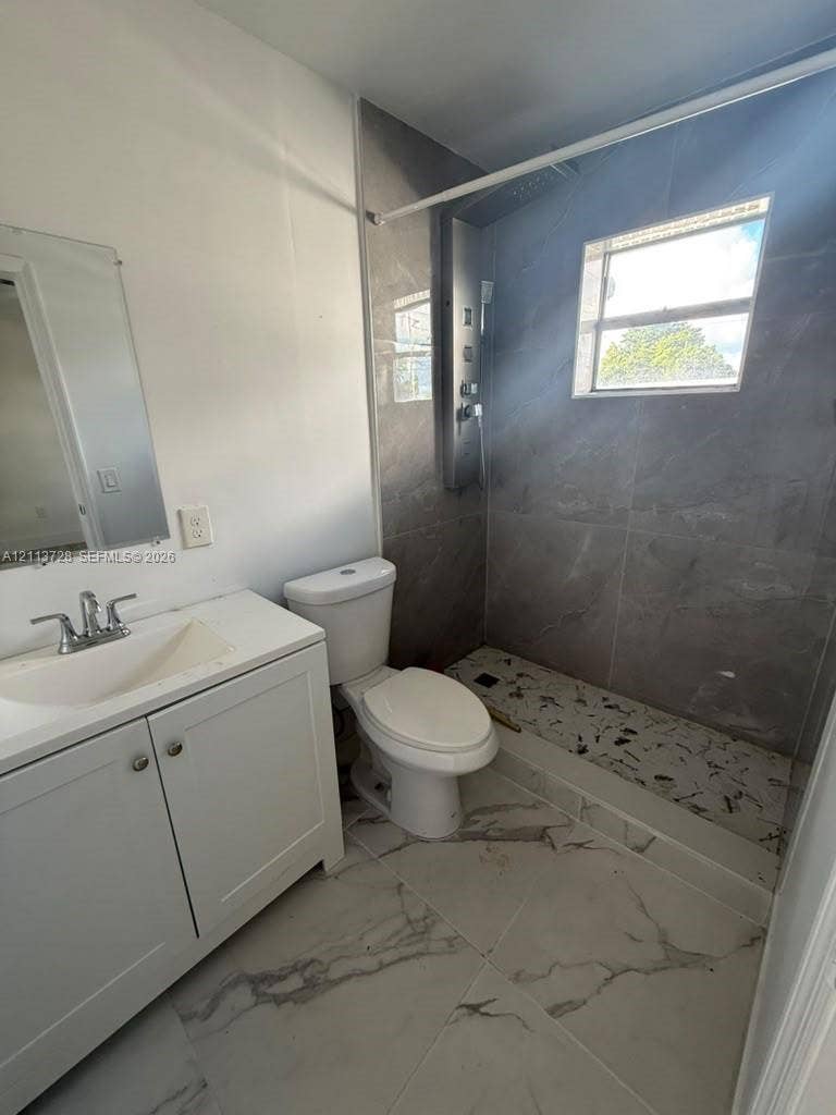 9200 SW 37th Street, Miami, FL 33165 Bathroom featuring large-format tile flooring, a white vanity with an integrated sink, and a walk-in shower with full-height tile surround, a built-in shower panel system, and a pebble-stone basin floor