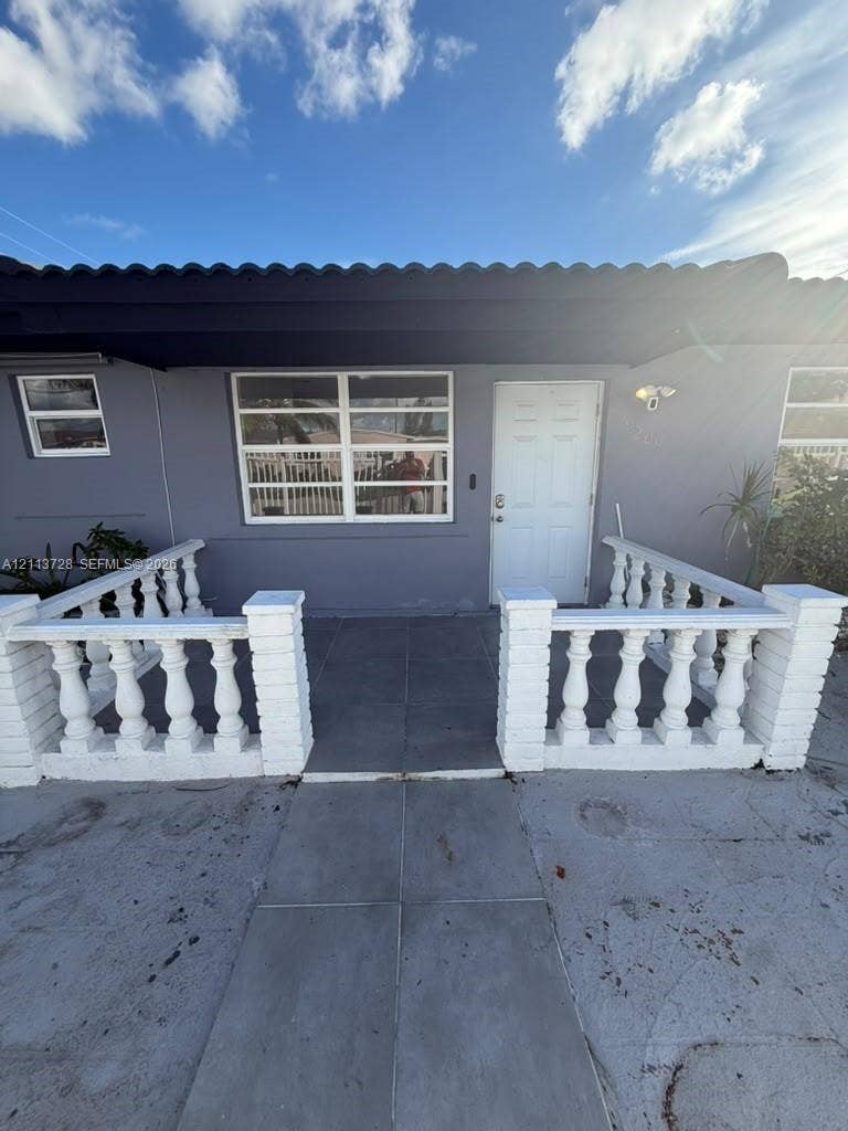 9200 SW 37th Street, Miami, FL 33165 Exterior facade featuring a concrete porch with white decorative balustrades, large horizontal-pane windows, and a solid-core entry door