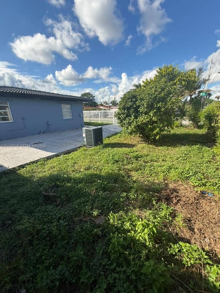 9200 SW 37th Street, Miami, FL 33165 Exterior grounds featuring a concrete patio, perimeter chain-link fencing, and mature vegetation