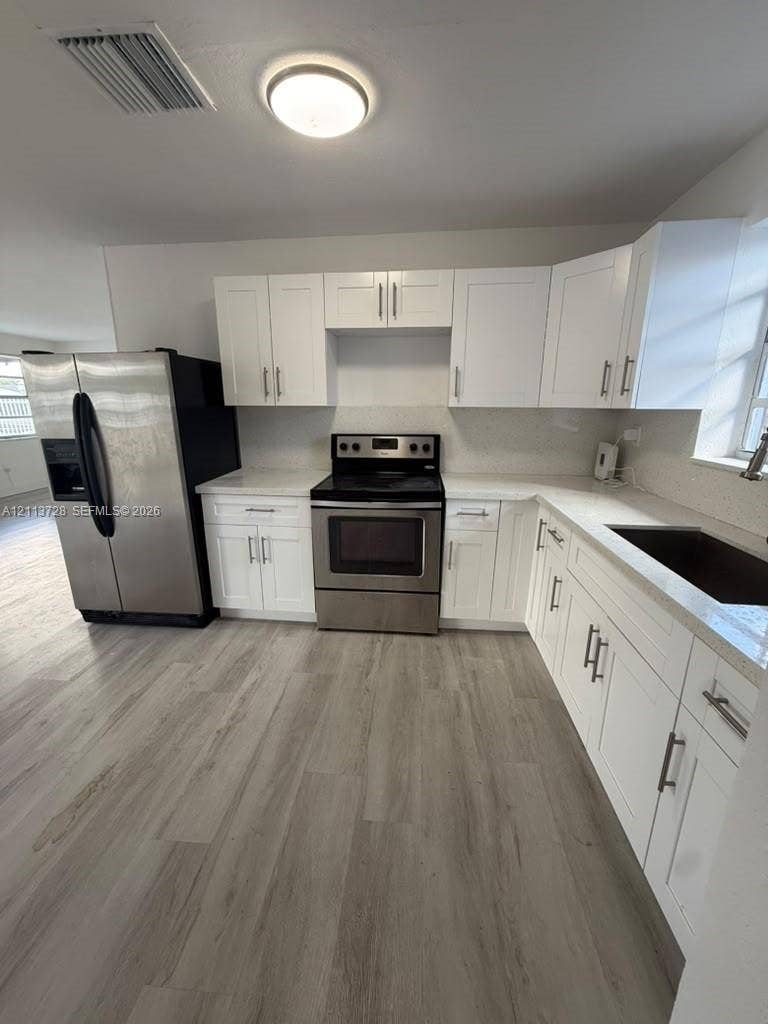 9200 SW 37th Street, Miami, FL 33165 Kitchen featuring white shaker-style cabinetry, stainless steel appliances, light stone-finish countertops, and wood-finish flooring