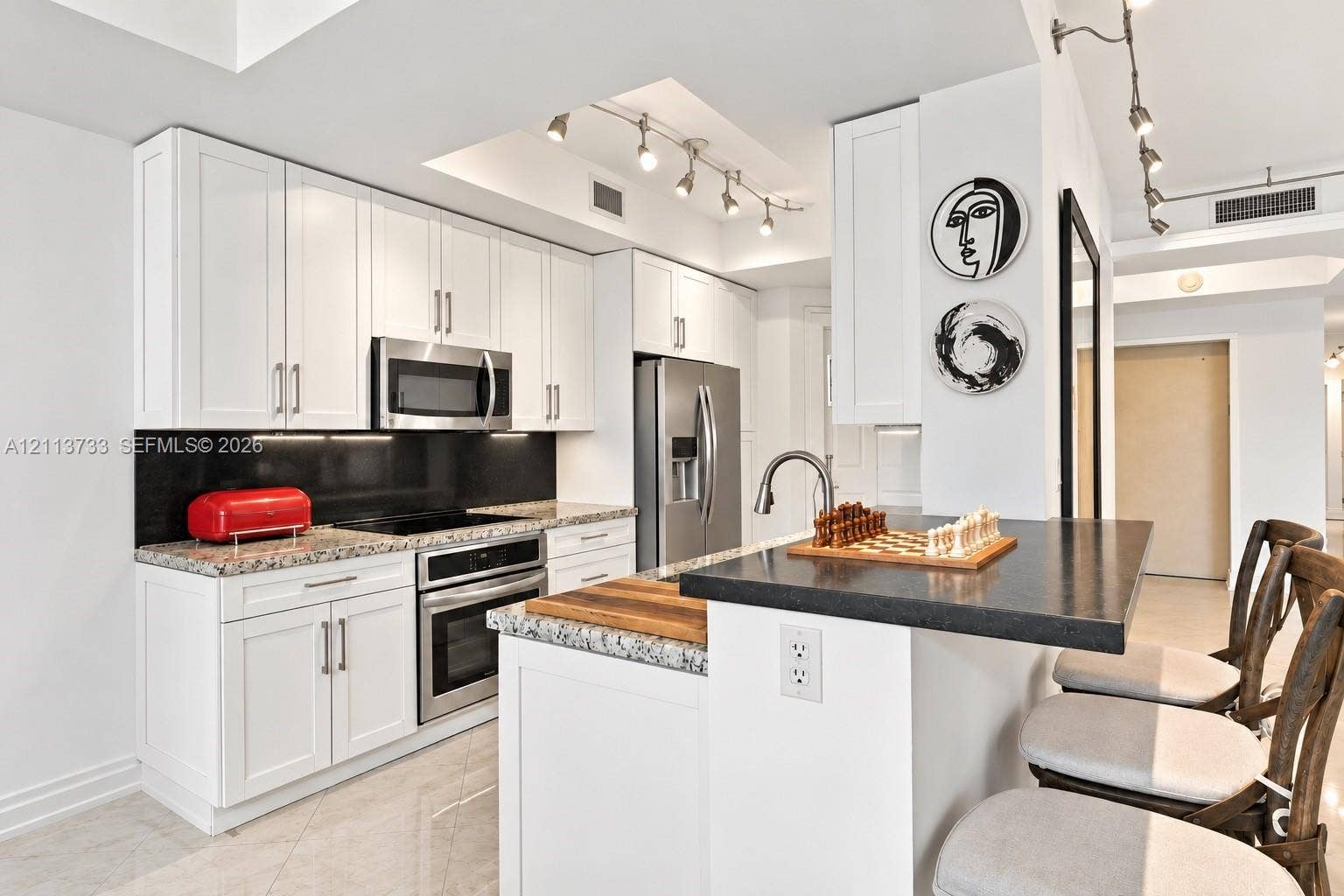 9751 E Bay Harbor Drive, #6A, Bay Harbor Islands, FL 33154 Kitchen featuring white shaker-style cabinetry, a stone-finish countertop, black backsplash, stainless steel appliances, and a breakfast bar with stone surfacing