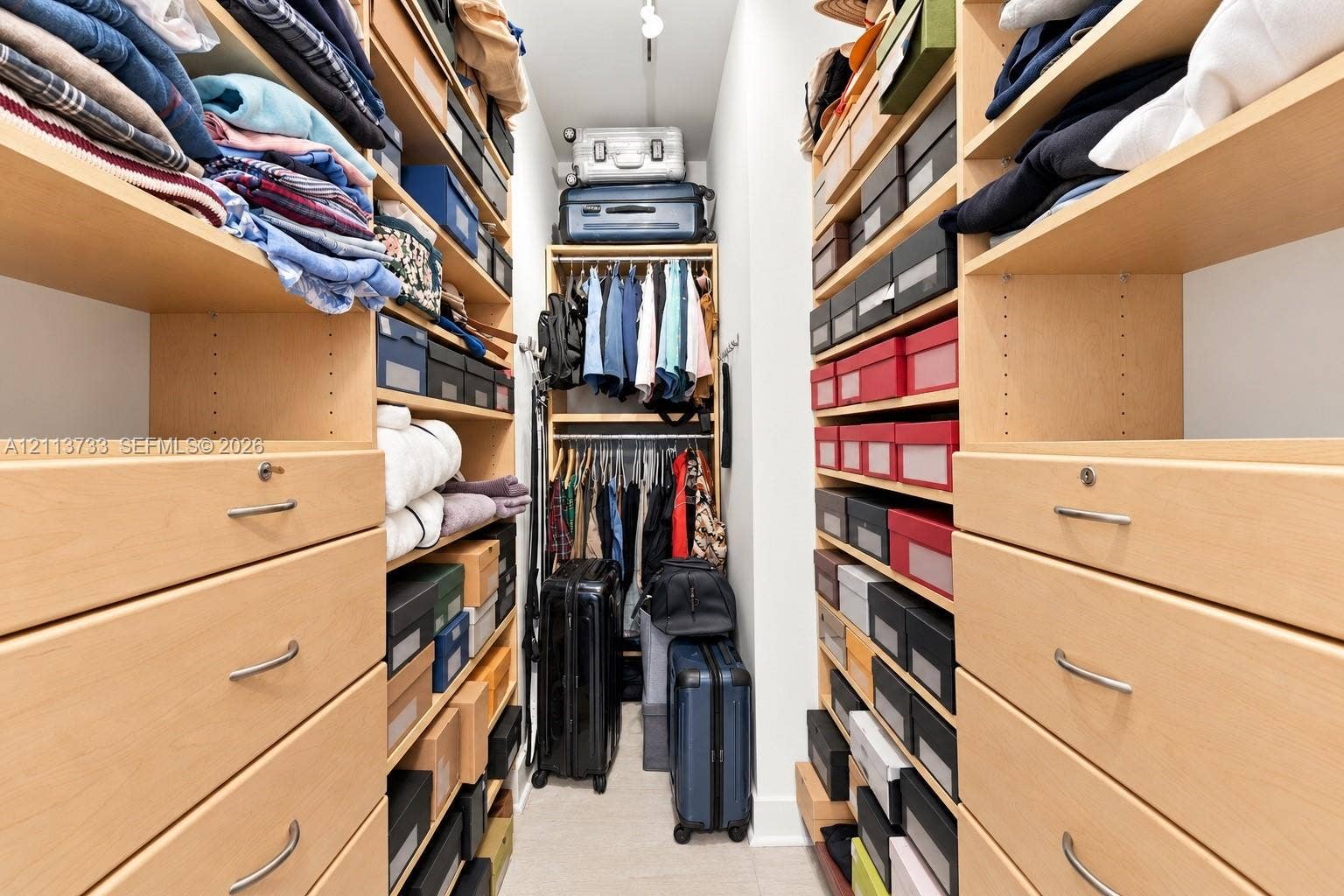 9751 E Bay Harbor Drive, #6A, Bay Harbor Islands, FL 33154 Custom reach-in closet featuring extensive built-in light wood cabinetry, multiple open shelving tiers, integrated drawers with metal hardware, and dual-level hanging rods