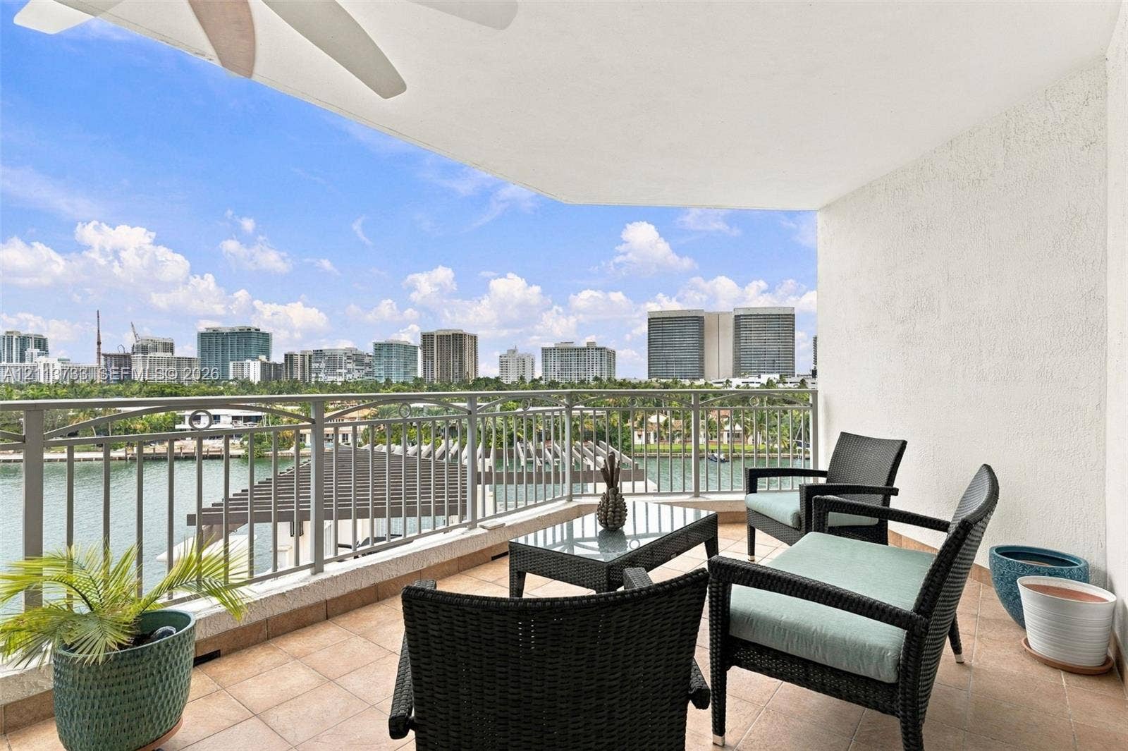 9751 E Bay Harbor Drive, #6A, Bay Harbor Islands, FL 33154 Covered balcony featuring tile flooring, a ceiling-mounted fan, and metal railings overlooking the water and urban skyline