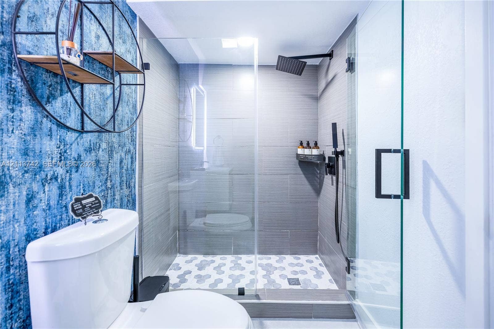 1930 NW 163rd St Road, Miami Gardens, FL 33054 Walk-in glass-enclosed shower featuring large-format gray wall tile, geometric pattern floor tile, and matte black rainfall shower fixture