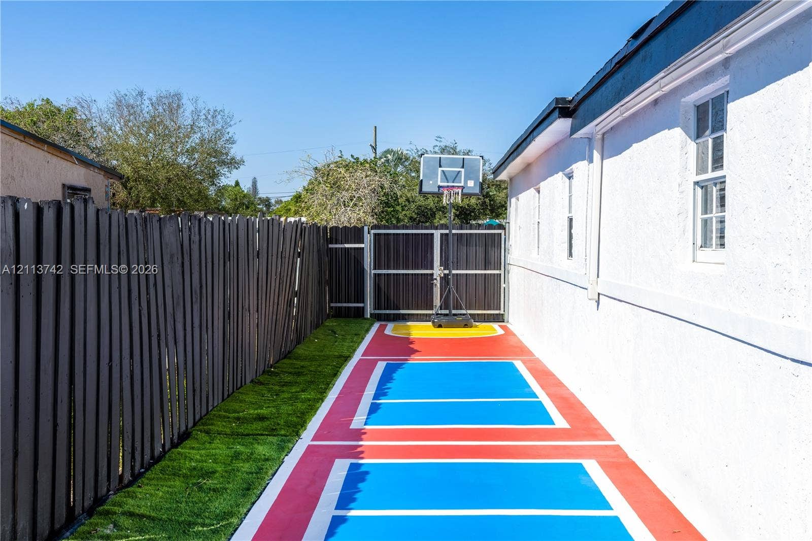 1930 NW 163rd St Road, Miami Gardens, FL 33054 Side yard featuring a painted sports court, synthetic turf, wood-finish perimeter fencing, and a gated entrance