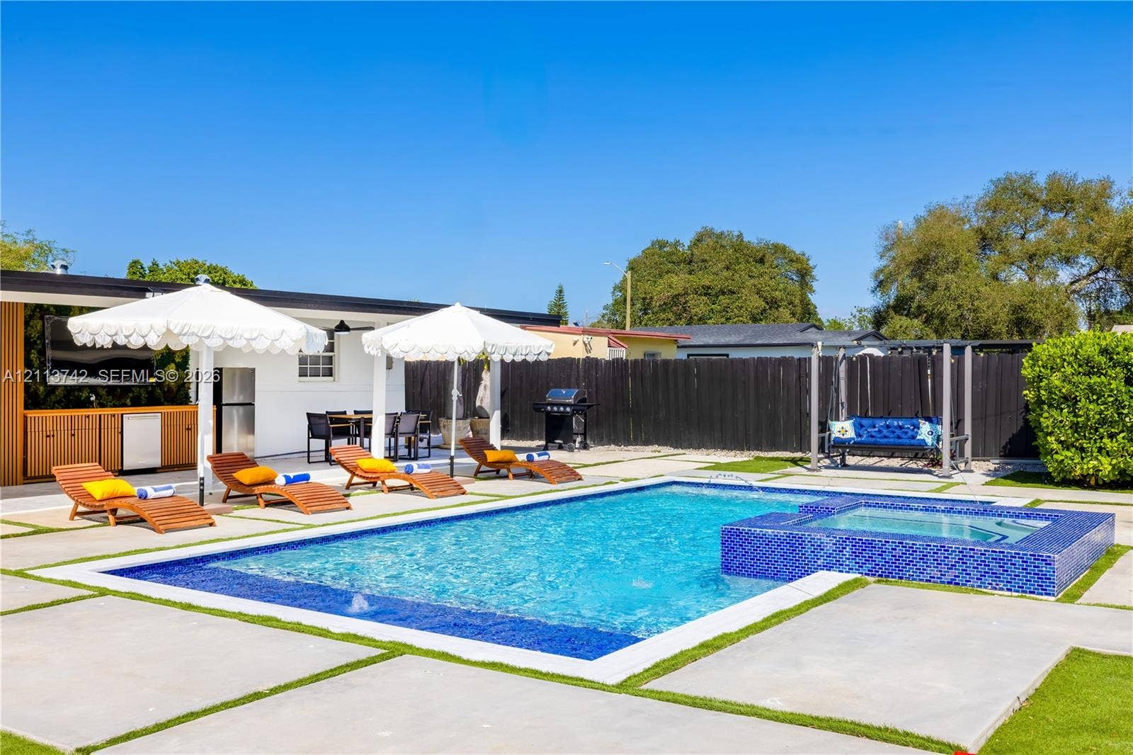 1930 NW 163rd St Road, Miami Gardens, FL 33054 Outdoor living space featuring a swimming pool, integrated tiled spa, concrete paver decking, and built-in outdoor kitchen cabinetry