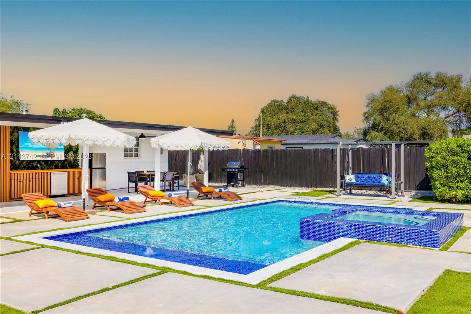 1930 NW 163rd St Road, Miami Gardens, FL 33054 Backyard featuring a swimming pool with a raised tiled spa, concrete paver decking with grass inserts, and a covered outdoor kitchen with built-in cabinetry