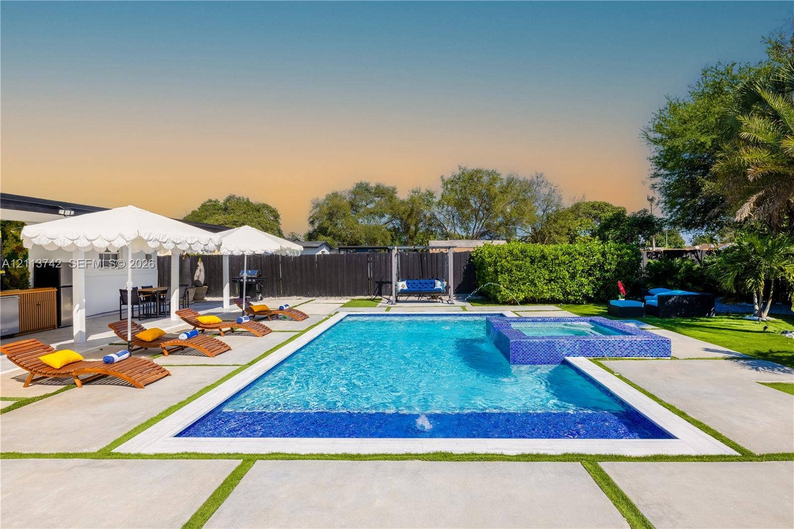 1930 NW 163rd St Road, Miami Gardens, FL 33054 In-ground swimming pool featuring a tiled spa, concrete paver decking, integrated turf ribbons, and a covered outdoor kitchen area
