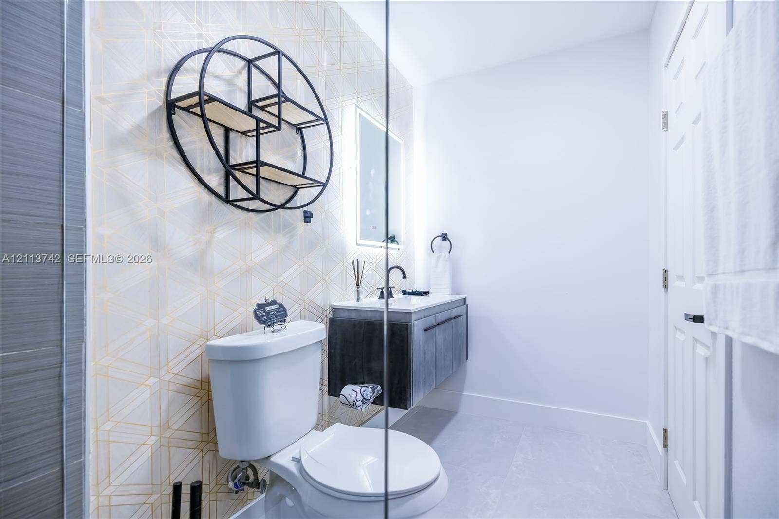 1930 NW 163rd St Road, Miami Gardens, FL 33054 Modern floating vanity with a dark wood-finish cabinet, geometric accent wall, illuminated mirror, and matte black hardware