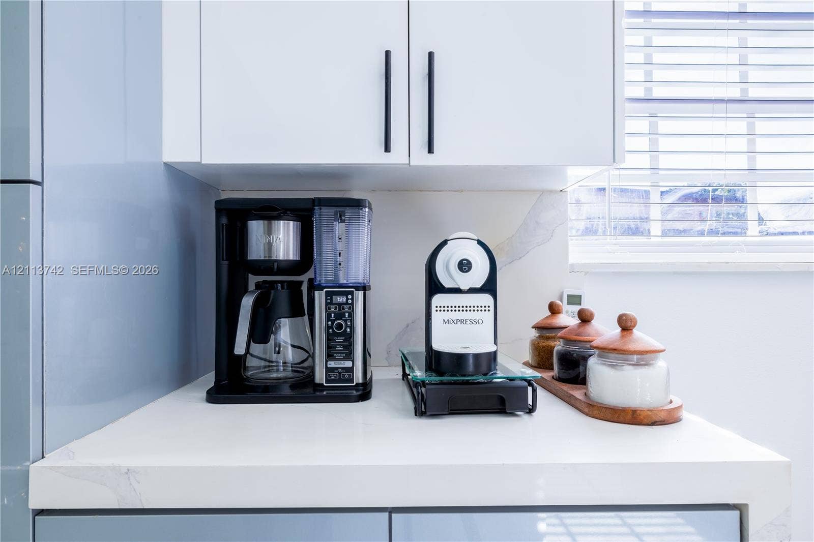 1930 NW 163rd St Road, Miami Gardens, FL 33054 White shaker-style cabinetry with matte black hardware, stone-surface countertop with subtle veining, and integrated horizontal window blinds