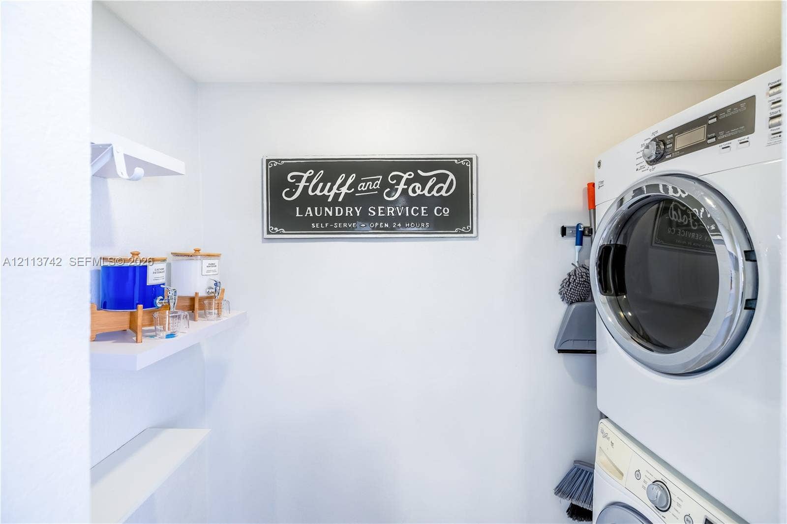 1930 NW 163rd St Road, Miami Gardens, FL 33054 Laundry area featuring a white stackable washer and dryer unit and built-in white wall-mounted shelving