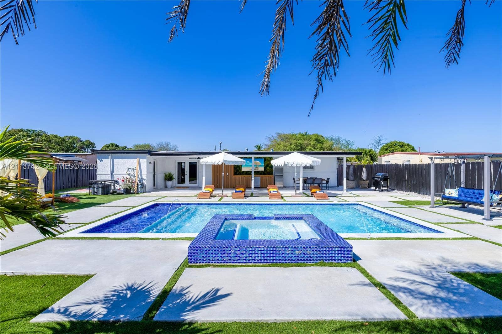 1930 NW 163rd St Road, Miami Gardens, FL 33054 Backyard featuring an in-ground pool with a raised spa, blue tile surround, concrete paver decking, and artificial turf accents