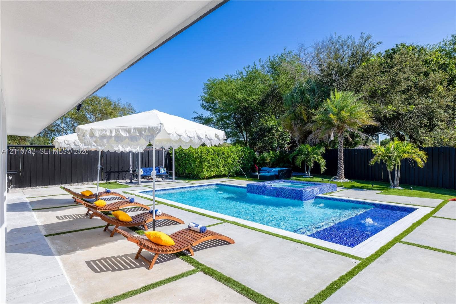 1930 NW 163rd St Road, Miami Gardens, FL 33054 Swimming pool with integrated spa, blue mosaic tile accents, concrete paver patio with turf inlays, and perimeter privacy fencing