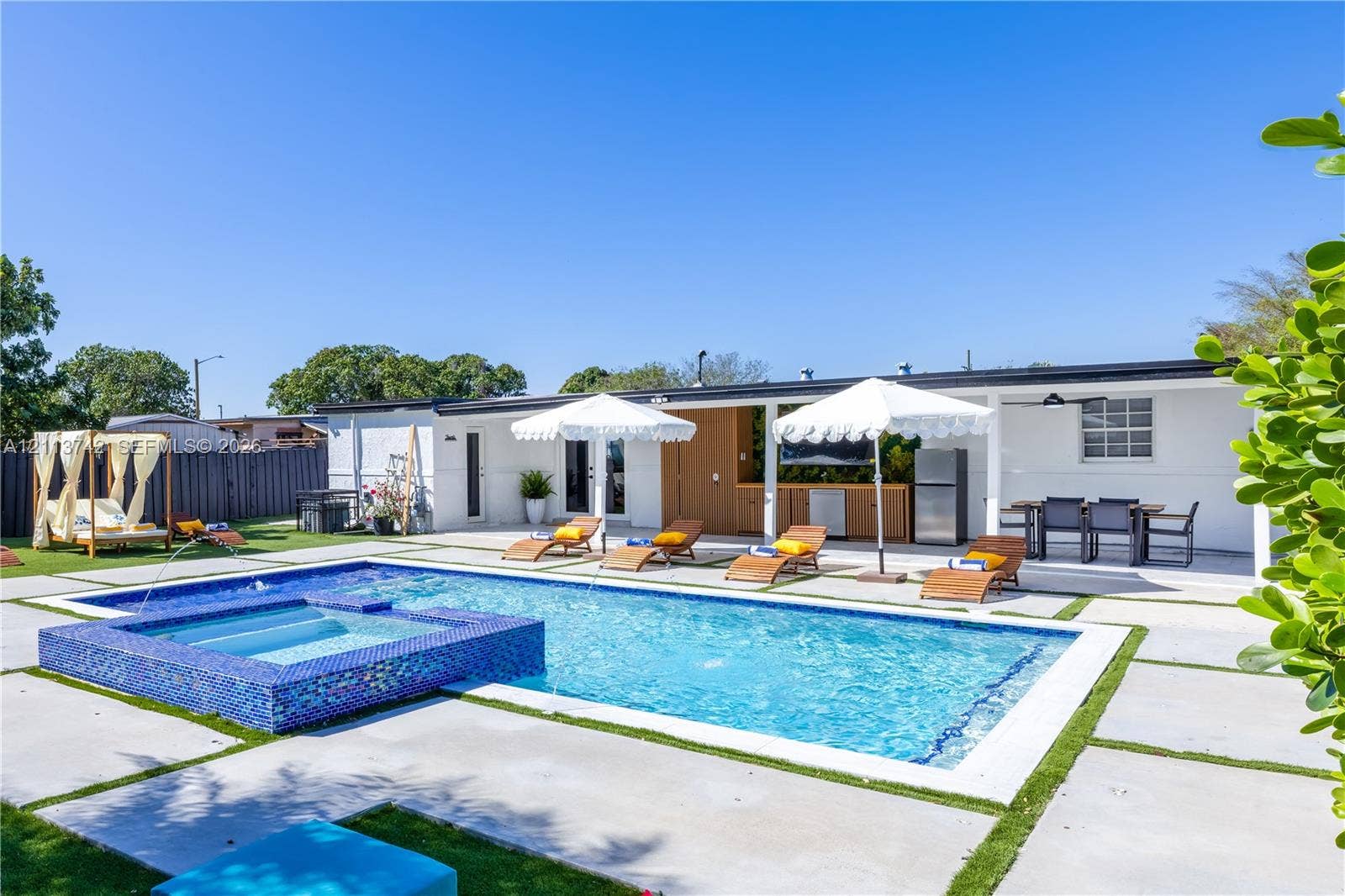 1930 NW 163rd St Road, Miami Gardens, FL 33054 Backyard featuring a swimming pool with a raised tiled spa, expansive concrete paver decking, and a covered outdoor kitchen area