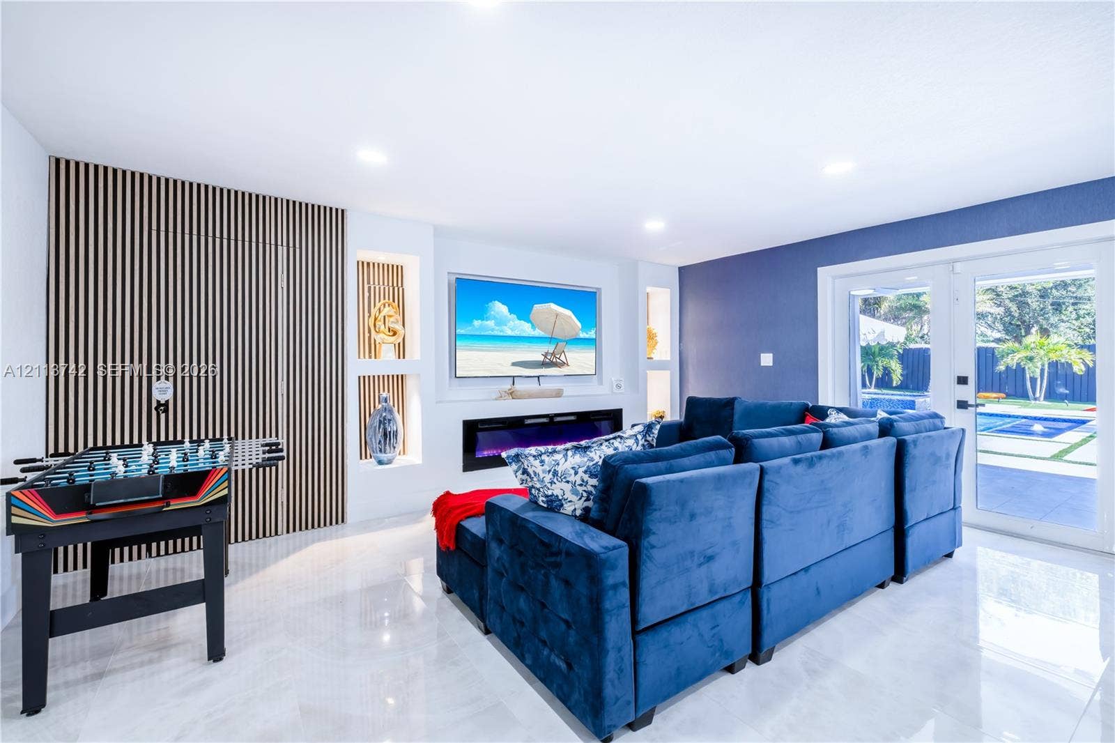 1930 NW 163rd St Road, Miami Gardens, FL 33054 Living area featuring large-format tile flooring, recessed lighting, a linear electric fireplace, built-in shelving, and vertical wood-slat wall accents