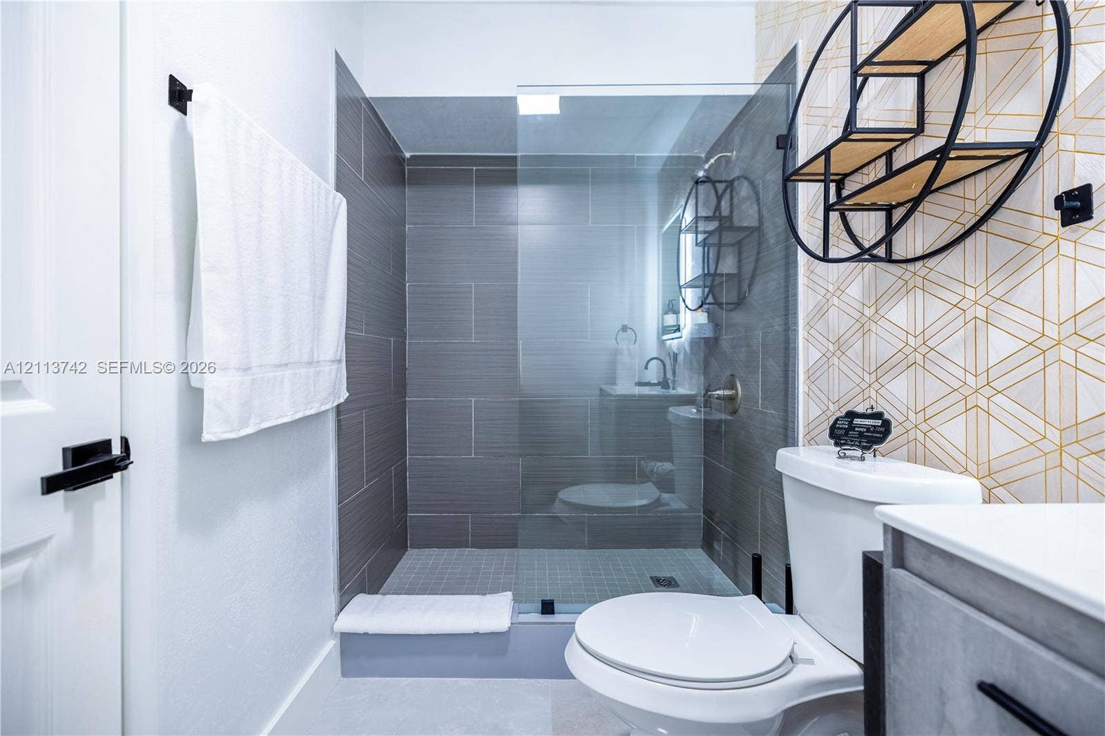 1930 NW 163rd St Road, Miami Gardens, FL 33054 Walk-in shower featuring gray horizontal tile surround, glass enclosure, and modern metal hardware, complemented by geometric patterned wall tile