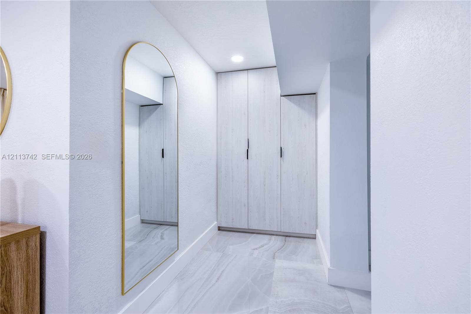 1930 NW 163rd St Road, Miami Gardens, FL 33054 Built-in cabinetry with light-toned finish, full-length arched wall mirror with metallic frame, recessed ceiling lighting, and large-format porcelain tile flooring