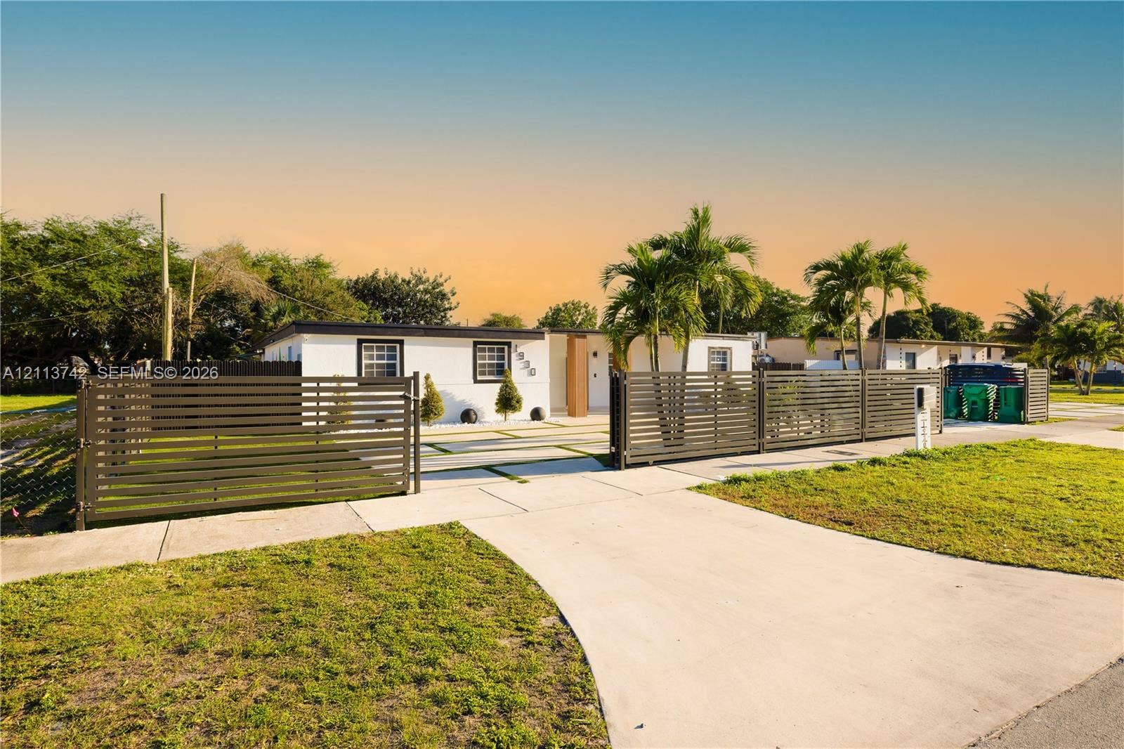 1930 NW 163rd St Road, Miami Gardens, FL 33054 Single-story exterior featuring white stucco finish, horizontal slat privacy fencing, concrete driveway, and palm tree landscaping