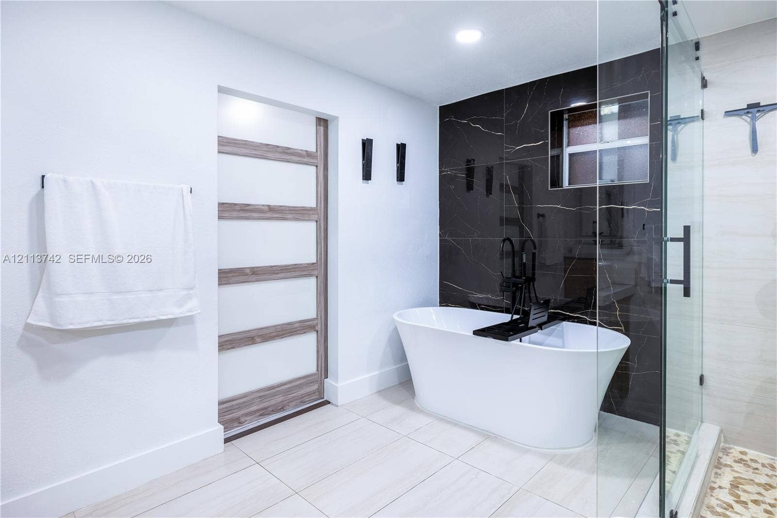 1930 NW 163rd St Road, Miami Gardens, FL 33054 Freestanding soaking tub with matte black floor-mounted faucet, dark stone-finish accent wall, glass-enclosed shower, and multi-panel door with wood-finish detailing
