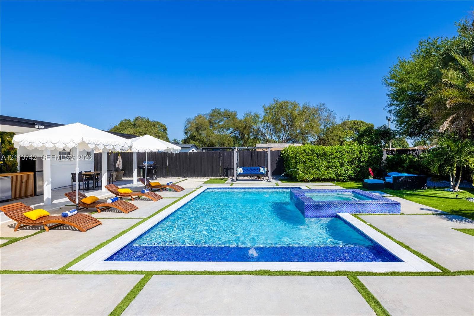 1930 NW 163rd St Road, Miami Gardens, FL 33054 In-ground pool with integrated spa and blue tile finish, surrounded by large-format concrete pavers with artificial turf inlay