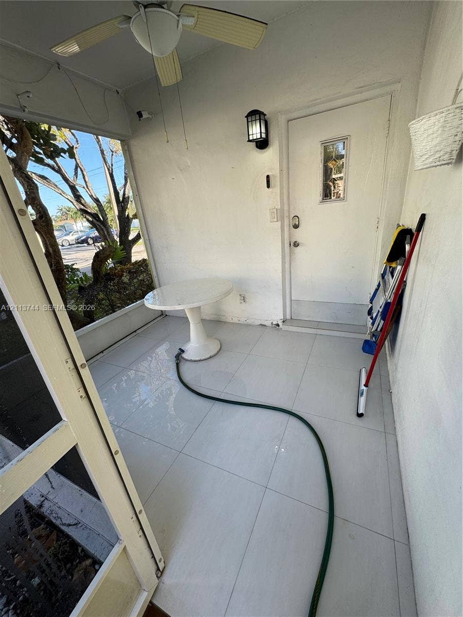 1501 Arthur Street, #1, Hollywood, FL 33020 Enclosed porch featuring large-format tile flooring, a ceiling fan with integrated lighting, a wall-mounted lantern-style sconce, and a front entry door with a decorative glass insert