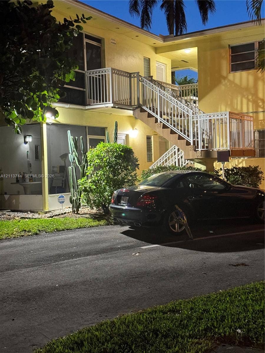 1501 Arthur Street, #1, Hollywood, FL 33020 Two-story exterior featuring a stucco facade, external staircase with white metal railings, and a ground-level screened enclosure