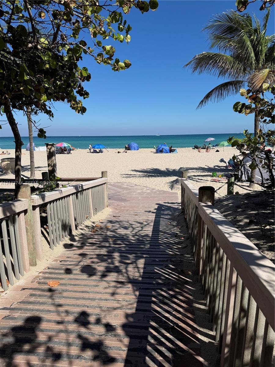 1501 Arthur Street, #1, Hollywood, FL 33020 Elevated wooden boardwalk featuring post-and-rail fencing, mature palm trees, and direct sand access to the coastline