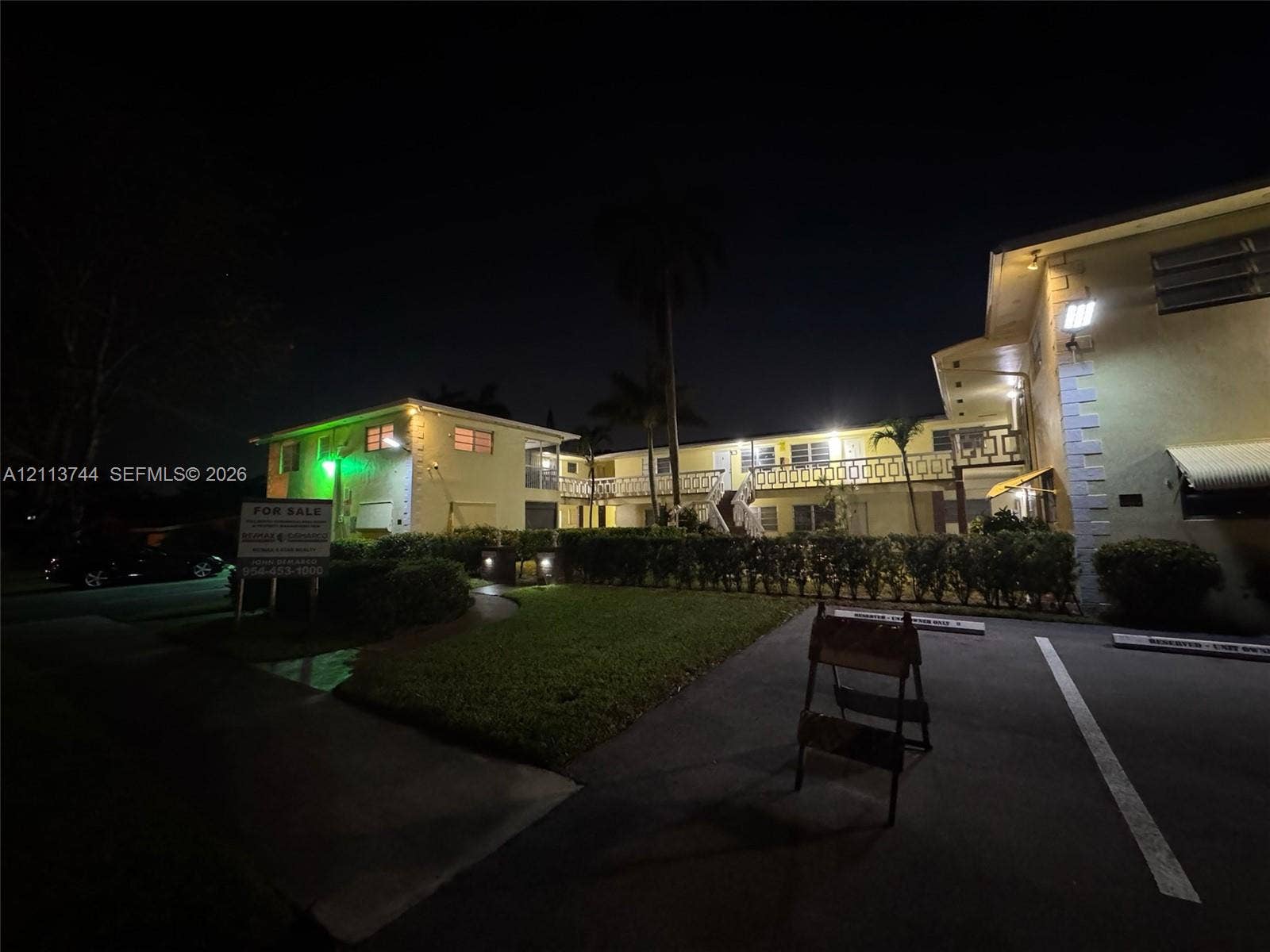 1501 Arthur Street, #1, Hollywood, FL 33020 Multi-story residential building featuring a stucco exterior, second-level balcony with decorative metal railing, manicured lawn, and dedicated asphalt parking area