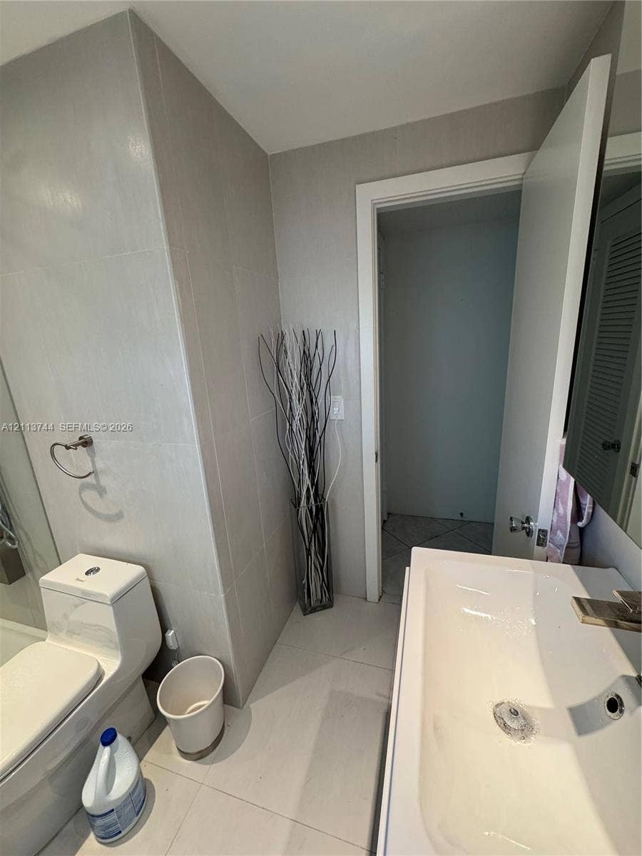 1501 Arthur Street, #1, Hollywood, FL 33020 Bathroom featuring large-format wall and floor tiling, a one-piece dual-flush toilet, a white ceramic wall-mounted sink, and a glass-enclosed shower