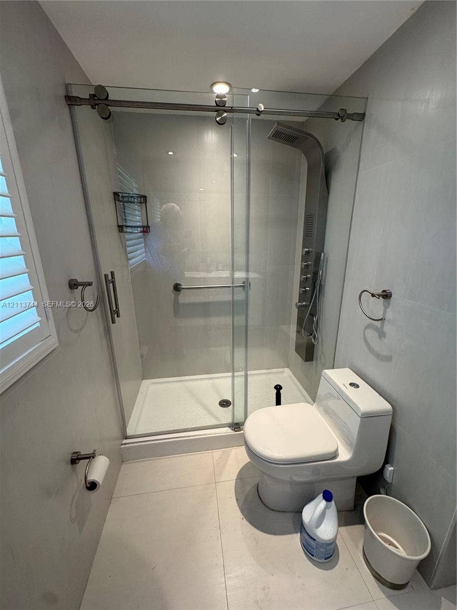1501 Arthur Street, #1, Hollywood, FL 33020 Walk-in shower with a sliding glass door, a wall-mounted stainless steel multi-head shower panel, integrated grab bar, large-format tile flooring, and a dual-flush toilet