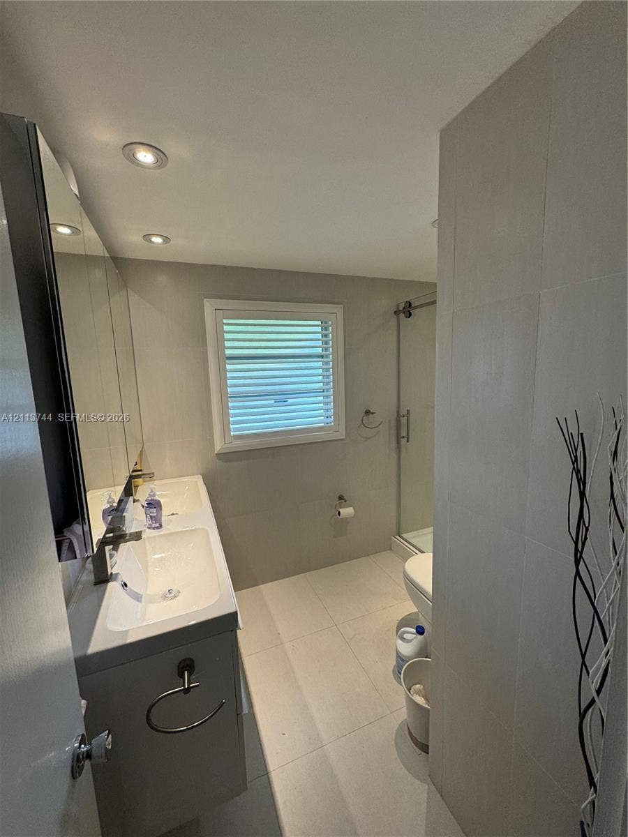 1501 Arthur Street, #1, Hollywood, FL 33020 Dual-sink vanity with a rectangular countertop, large-format tile flooring, wall-to-wall mirror, recessed lighting, and a glass-enclosed shower