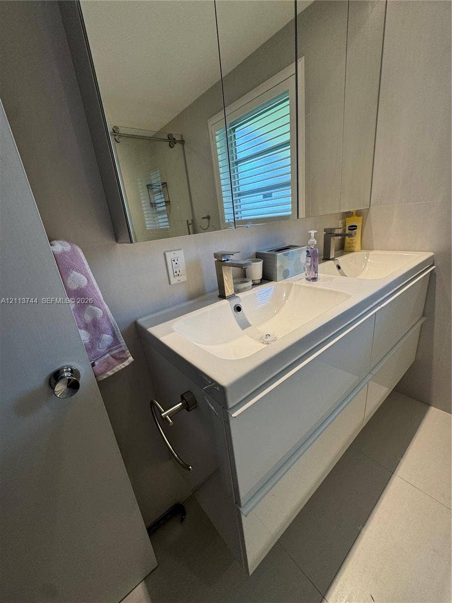 1501 Arthur Street, #1, Hollywood, FL 33020 Floating dual-sink vanity featuring a high-gloss finish, integrated basins, and minimalist chrome faucets, complemented by a wide medicine cabinet and large-format floor tiling