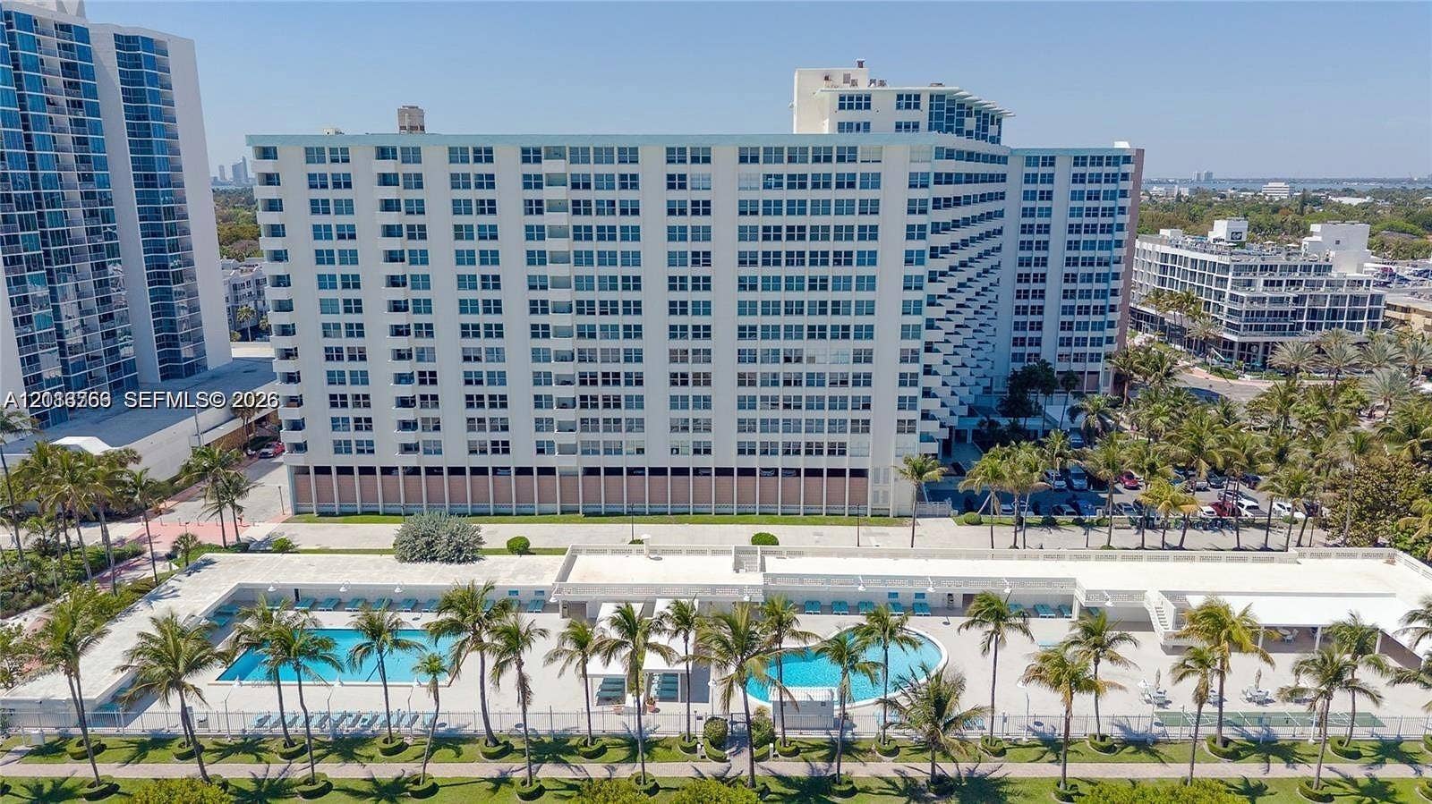 2899 Collins Avenue, #1429, Miami Beach, Miami Beach, FL 33140 High-rise residential exterior featuring a multi-story facade, dual ground-level swimming pools, paved pool deck, and mature palm tree landscaping