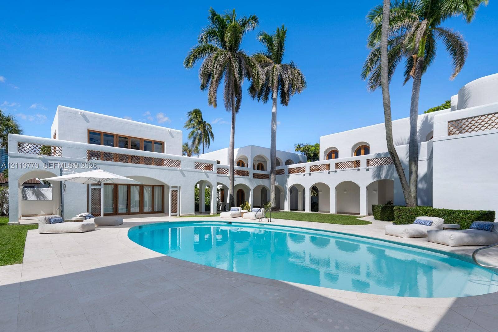 387 Ocean Boulevard, Golden Beach, Golden Beach, FL 33160 Stucco exterior featuring arched covered loggias, second-story balconies with decorative latticework, oval swimming pool, and stone-finished patio