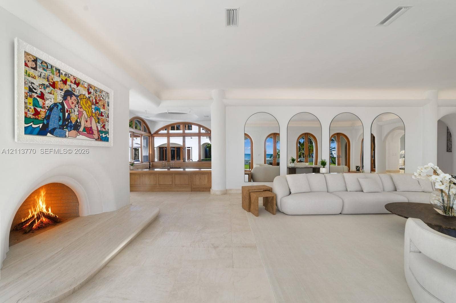 387 Ocean Boulevard, Golden Beach, Golden Beach, FL 33160 Open-concept living space featuring stone flooring, a recessed arched fireplace with an extended stone hearth, and floor-to-ceiling arched mirrors